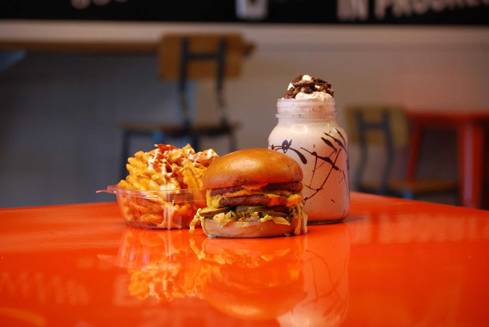 Cheeseburger with fries and a milkshake on a vibrant orange table.